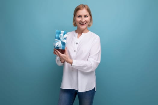 blond mature woman holding gift box on studio background.