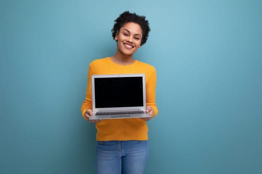 pretty young brunette latin female adult in yellow sweater showing laptop screen with mockup for advertising.