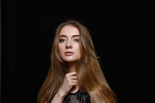 brunette woman with long hair in black dress looking at the camera on black background