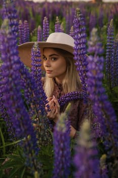 A beautiful woman in a straw hat walks in a field with purple flowers. A walk in nature in the lupin field.