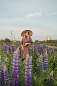 A beautiful woman in a straw hat walks in a field with purple flowers. A walk in nature in the lupin field.