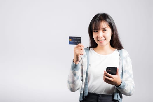 Woman excited smiling hold mobile phone and plastic debit credit bank card for payment studio shot isolated white background, happy young female using smartphone buy and pay online shopping