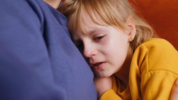 Close-up portrait of upset child little girl kid crying with tears flowing down on her cheek, toddler lies on mother at home. Mom hugs, embrace, takes pity on her daughter. Quarrel, bullying at school