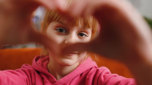 I love you. Child kid girl makes symbol of love, showing heart sign to camera, express romantic feelings, express sincere positive feelings. Charity, gratitude, donation. Female teen toddler at home