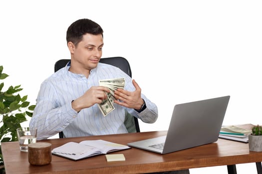 young handsome businessman working on laptop and holding money while sitting on chair at desk.
