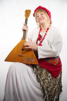 Cheerful funny adult mature woman solokha with musical balalaika. Female model in clothes of national ethnic Slavic style. Stylized Ukrainian, Belarusian or Russian woman poses in comic photo shoot
