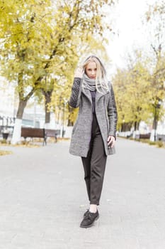 A young blonde walks through the autumn city in a gray coat. The concept of urban style and lifestyle