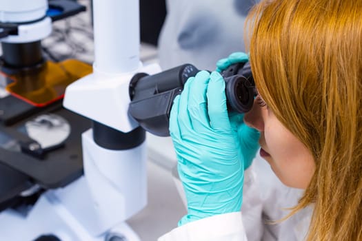 A female scientist is conducting biological analysis in a laboratory, while peering through a microscope