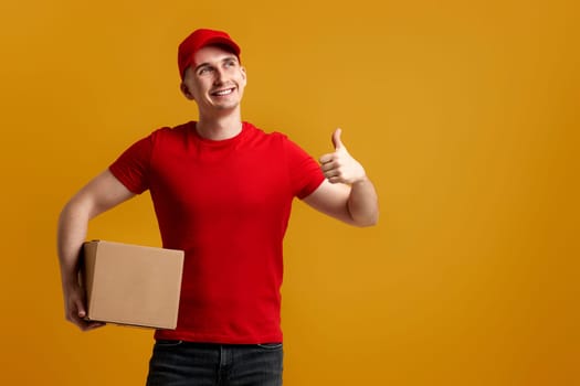 Delivery man employee in red cap, red t-shirt holding cardboard box isolated on yellow background
