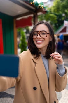 Beautiful woman using mobile phone for video call outdoors. Smiling girl looking smart phone screen in a city street. Happy smiling woman chatting on smartphone warm autumn day