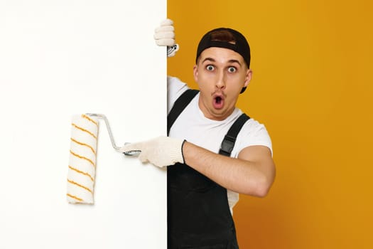surprised young man in working clothes painting white walls in the room. copy space for text