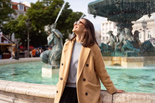 Female tourist enjoying in Lisbon downtown, Portugal. Sunny day. Travel Europe concept. woman dressed stylish coat sitting in front of baroque fountains in Praca Dom Pedro IV or Rossio Square, Lisbon.