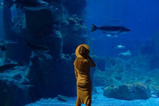 A young woman touches a stingray fish in an oceanarium tunnel.