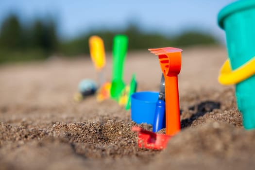 Children's toys for playing on the sand. Plastic bucket and rake on the beach at sunset. The concept of summer, family holidays and vacations. Various plastic toys for children.