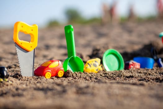 Children's toys for playing on the sand. Plastic bucket and rake on the beach at sunset. The concept of summer, family holidays and vacations. Various plastic toys for children.