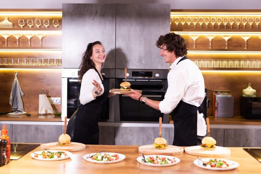 Happy chef and his colleague standing at kitchen and looking at camera - food and restaurant