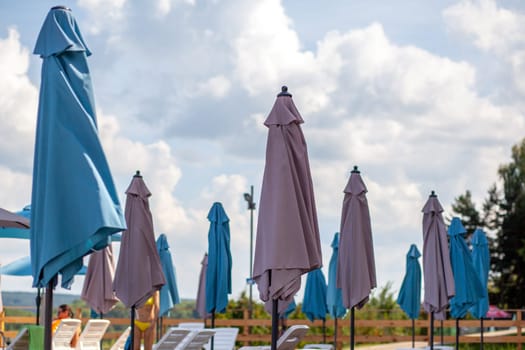 Folded beach umbrellas. Preparing the beach for the new opening season. Lots of beach umbrellas next to the water pool. The concept of tourist vacation and vacation.