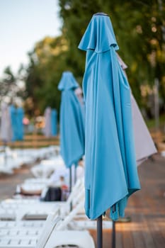 Folded beach umbrellas. Preparing the beach for the new opening season. Lots of beach umbrellas next to the water pool. The concept of tourist vacation and vacation.