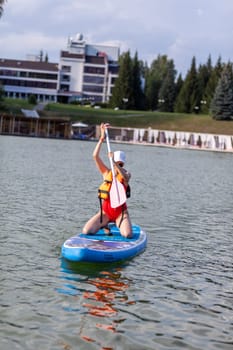 A girl in a life jacket swims on a SUP board. SUP board Stand up paddle girl boarding on lake standing happy on blue water.