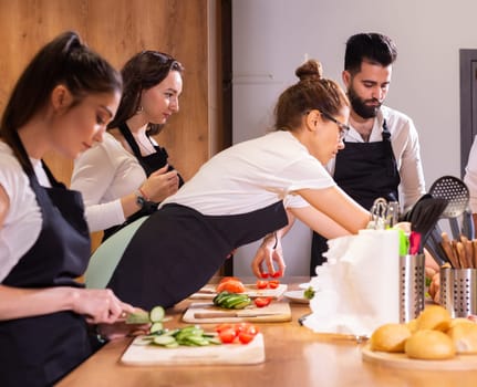 Cooking course concept - senior male chef in cook uniform teaches young people cooking class students to prepare and mix ingredients for dishes in restaurant kitchen