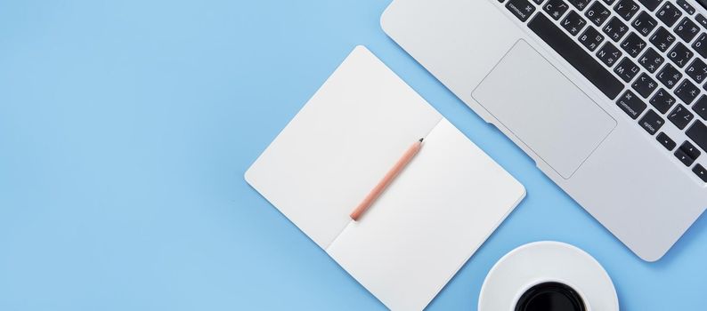 Girl write on open white book or accounting on a minimal clean light blue desk with laptop and accessories, copy space, flat lay, top view, mock up