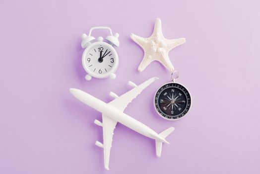 World Tourism Day, Top view flat lay of minimal toy model plane, airplane, starfish, alarm clock and compass, studio shot isolated on a purple background, accessory flight holiday concept