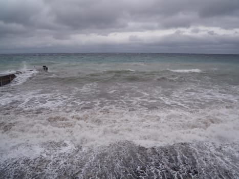 View of storm seascape. Dark moody sky over the gray sea. Waves and dark clouds in stormy day