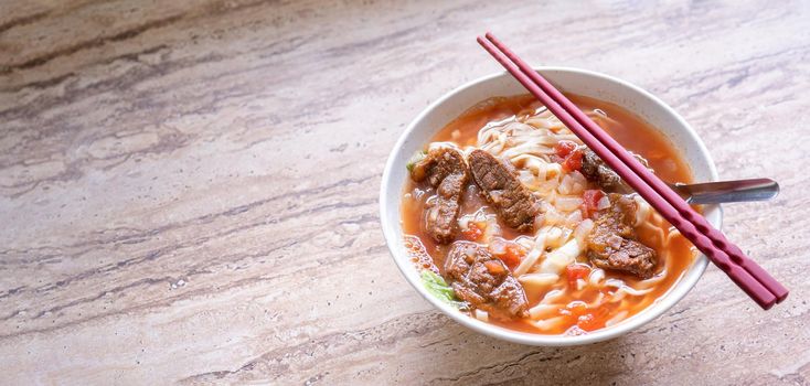 Beef noodle ramen meal with tomato sauce broth in bowl on bright wooden table, famous chinese style food in Taiwan, close up, top view, copy space