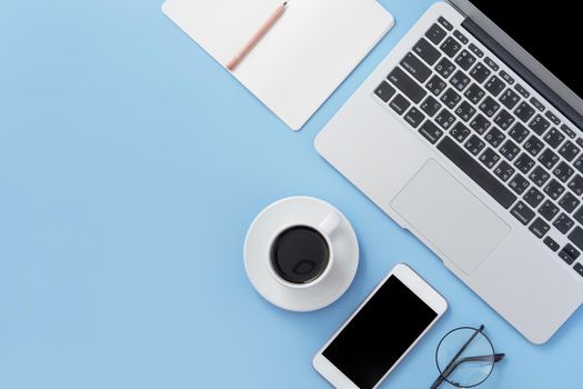 Business concept. Clean bright light blue office table desk, minimal style with laptop coffee and smart phone, copy space, top view, flat lay, mockup