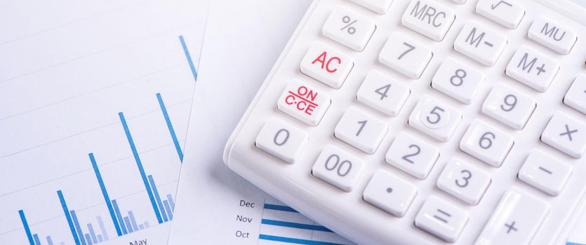 White calculator and report with chart and graph, concept of annual financial profit overview, banking and investment, copy space, macro, close up