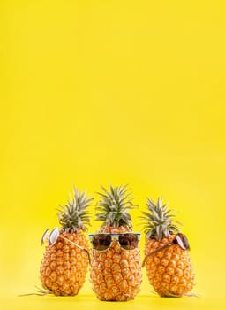 Creative pineapple looking up with sunglasses and shell isolated on yellow background, summer vacation beach idea design pattern, copy space close up