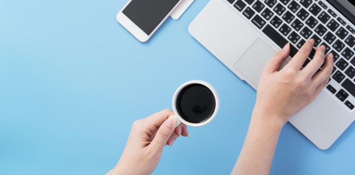 Woman surf internet for job hunting. Freelancer blog writer typing on a cleam light blue desk with coffee, copy space, flat lay, top view, mock up