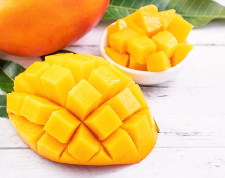 Beautiful chopped mango with green leaves on bright white color timber background. Above Top view, flat lay, copy space, close up. Tropical fruit concept.