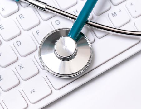 Stethoscope on computer keyboard on white background. Physician write medical case long term care treatment concept, close up, macro, copy space
