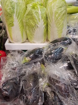 A lot of Chinese cabbage and eggplant in plastic bags on the counter of the vegetable market, vertical.