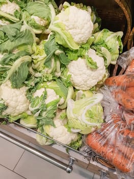 Close-up of cauliflower and fresh raw carrots in plastic bags on the counter in the store. Retail sale of vegetables.