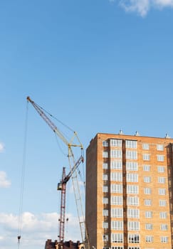 Construction of a new apartment building, against the blue sky, a high-rise construction crane. Vertical photo