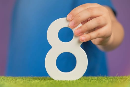 Number 8 in hand. A hand holds a white number eight on a purple background, eight percent per annum. The concept of international women's day on March 8. Advertising banner or greeting card