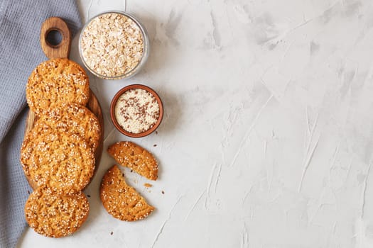 Oatmeal cookies with sesame seeds and flax seeds on a gray background with a jar of oatmeal and textiles. copy space