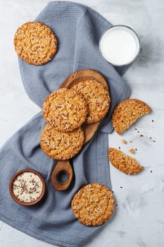 Oatmeal cookies with sesame seeds and flax seeds on a gray background with a jar of oatmeal and a glass of milk.