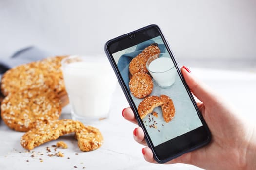 A woman takes a photo of oatmeal cookies on her phone. food photo concept