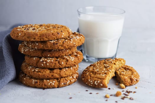 Oatmeal cookies with sesame seeds and flax seeds with a glass of milk on a gray background.