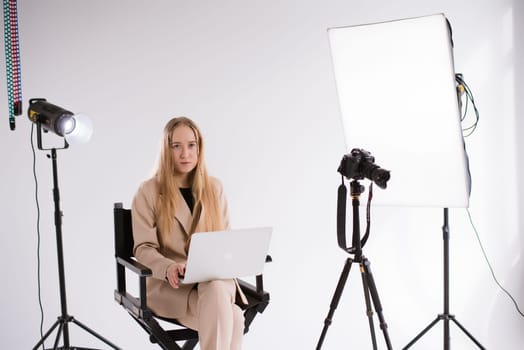 A business woman videographer producer assistant in a suit is working, typing on a laptop and sitting on a chair. Video Production studio, tripod camera