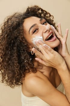 Woman beauty face close-up applying foam to wash and cleanse skin with fingers of her hand, nail and hair health, hair dryer style curly afro hair, body and beauty care concept. High quality photo