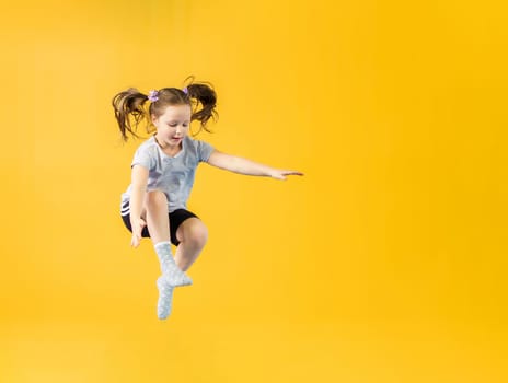 Happy little girl jumping on a yellow background