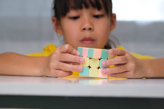 Asian little cute girl holding Rubik's cube in her hands and playing with it. Rubik's cube is a game that increases intelligence for children. Educational toys for children