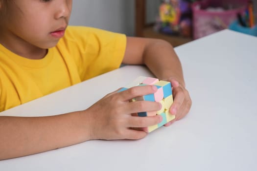 Asian little cute girl holding Rubik's cube in her hands and playing with it. Rubik's cube is a game that increases intelligence for children. Educational toys for children