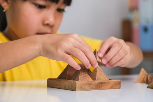 Asian cute little girl playing with wooden toy jigsaw puzzle pyramid on table. Healthy children training memory and thinking. Wooden puzzles are games that increase intelligence for children. Educational toys for children.