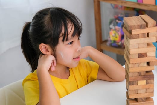 Cute Asian siblings having fun playing Jenga together. Two children playing Jenga board game on table in room at home. Wooden puzzles are games that increase intelligence for children. Educational toys for children.