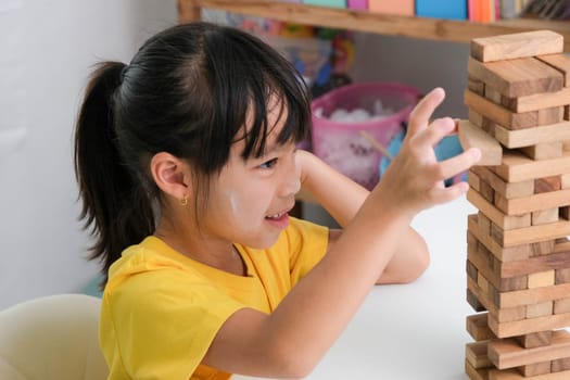 Cute Asian siblings having fun playing Jenga together. Two children playing Jenga board game on table in room at home. Wooden puzzles are games that increase intelligence for children. Educational toys for children.